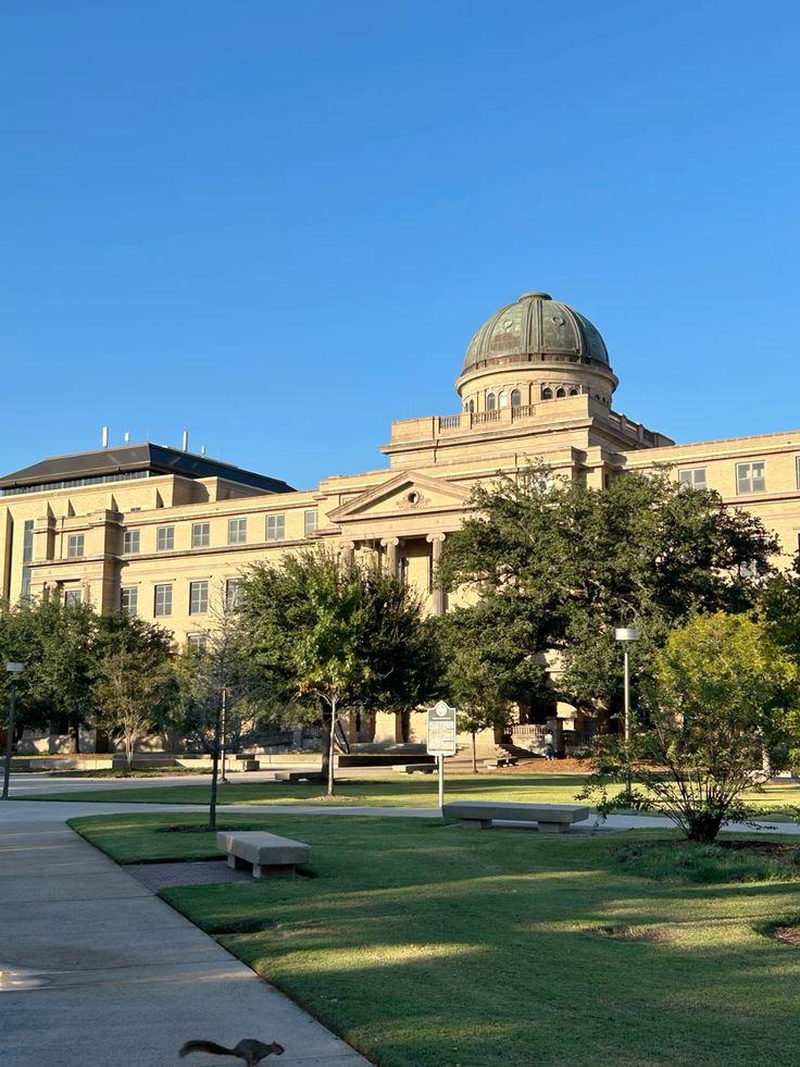 A campus academic building with a domed roof, surrounded by trees and lawns.